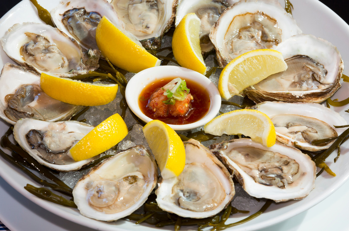 strange French Christmas foods-a plate of fresh raw oysters on ice with lemon wedges and hot sauce