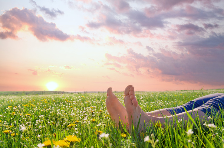 Earthing health benefits-a man lying bare feet on spring grass and flowers