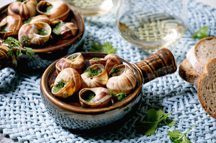 unique christmas customs in france by region-escargots de bourgogne-snails with herbs butter-in traditional french ceramic pan with bread-glass of white wine-on blue straw napkin