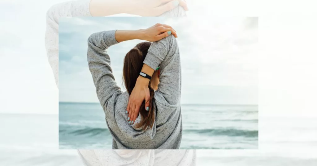 woman doing a triceps stretch while standing on the beach