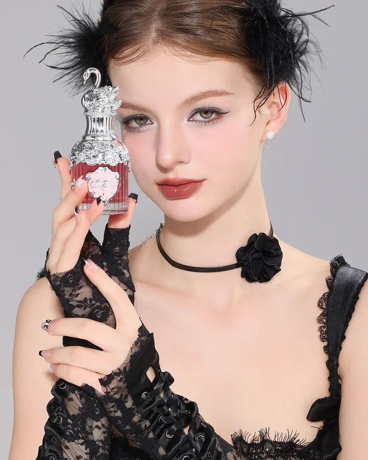 a young girl in black outfit holding a perfume in a swan shaped glass bottle